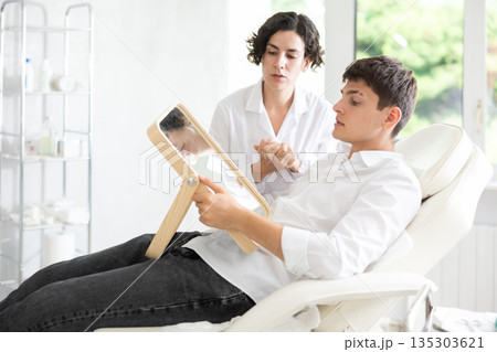 Young man having consultation about face aesthetic while looking in the mirror 135303621
