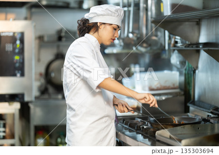Young woman cook in kitchen is working near stove 135303694