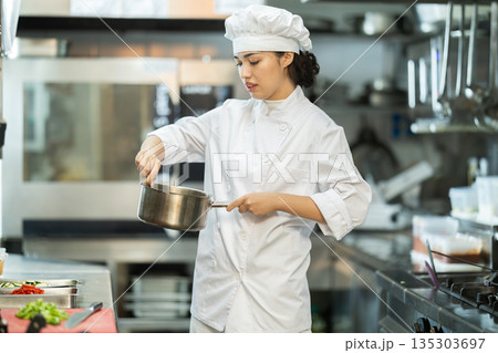 Young female cook mixing something in little saucepan 135303697