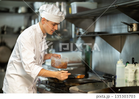 Young man cook in kitchen is working near stove Young man cook in kitchen is working near stove 135303703