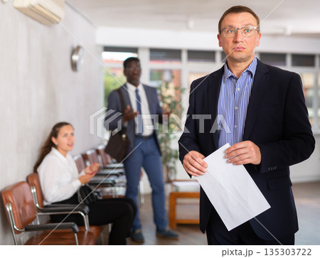 Upset middle-aged man standing in waiting room with his back to person who is shouting at him Upset middle-aged man standing in waiting room with his back to person who is shouting at him 135303722