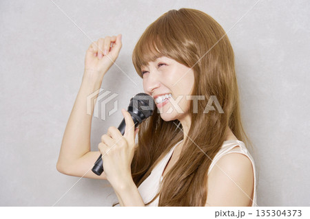 マイクを持って歌うミドルエイジの女性　ポートレート　グレー背景 135304373