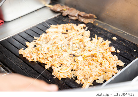 A person is cooking meat on a grill 135304415
