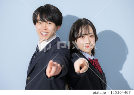 水色背景で並ぶ高校生の男女 女子高生と男子高生の2人の見上げる進路や未来や目標、合格を目指す指を差す 水色背景で並ぶ高校生の男女 女子高生と男子高生の2人の見上げる進路や未来や目標、合格を目指す指を差す 135304467