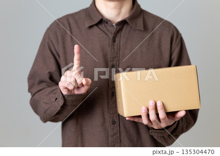 段ボール箱の荷物を持って人差し指を立てるミドル男性 135304470
