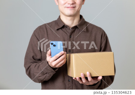 段ボール箱の荷物とスマホを持つミドル男性 段ボール箱の荷物とスマホを持つミドル男性 135304623