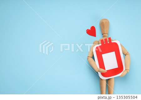 Wooden figure embraces a red blood bag on light blue background Wooden figure embraces a red blood bag on light blue background 135305504