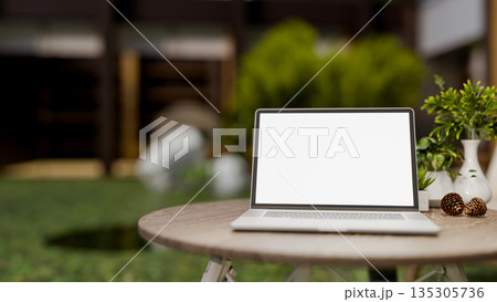 White screen laptop with decor acorn and flower vase on round wooden table in a garden or backyard. 135305736