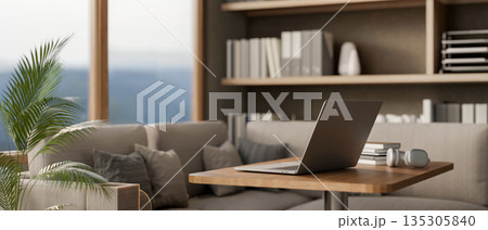 Laptop with books and headphone on wooden stool table beside fabric sofa in a living room or office. 135305840