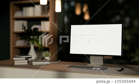 Blank screen computer with book and flower vase on wooden table in a living room or bedroom at night 135305844
