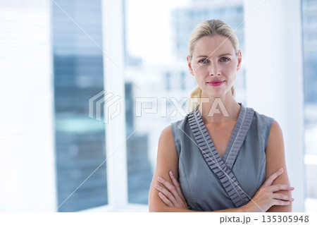 Female professional crossing arms while standing by glass windows in high-rise office, copy space 135305948