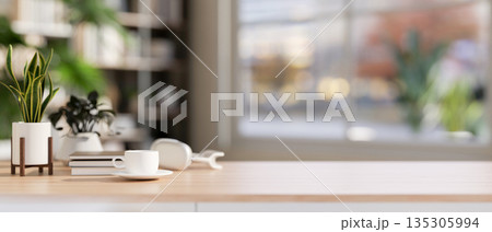 Coffee cup with headphone aside books and potted plant on wooden table in bright living room or cafe 135305994