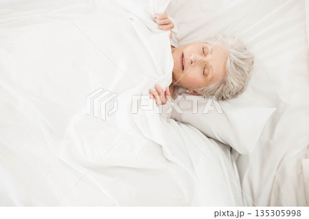 Senior woman sleeping quietly in bedroom at home under white sheets and blanket, copy space 135305998