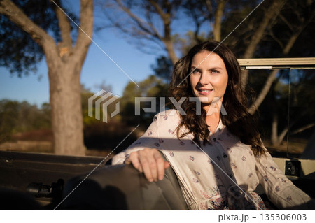 Woman leaning against off-road vehicle seat in wooded clearing in golden light, copy space Woman leaning against off-road vehicle seat in wooded clearing in golden light, copy space 135306003