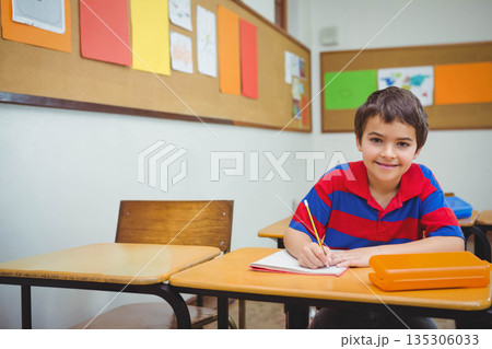 Primary schoolboy writing in notebook with yellow pencil at desk in classroom, copy space 135306033