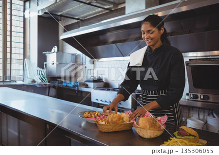 Indian chef in chef coat arranging bread and pastry baskets on table in kitchen, copy space 135306055