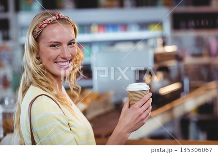 Woman smiling and holding ribbed paper coffee cup at cafe counter with espresso machine, copy space 135306067