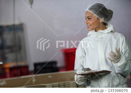 Female lab technician smiling and holding clipboard in lab wearing protective gear, copy space Female lab technician smiling and holding clipboard in lab wearing protective gear, copy space 135306070