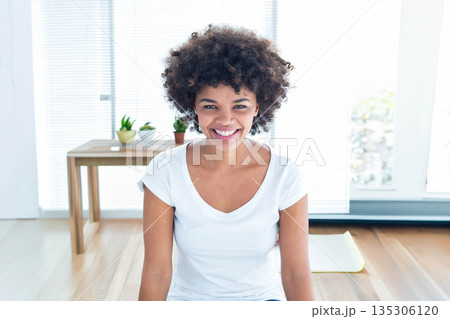 African American woman sitting on yoga mat in home studio by window with blinds, table, plants African American woman sitting on yoga mat in home studio by window with blinds, table, plants 135306120