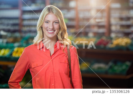 Woman smiling in red-orange shirt carrying purse strap at grocery store bins of produce 135306126
