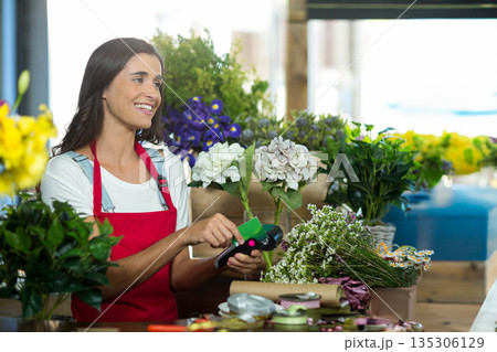 Female florist trimming hydrangea stem with green-handled cutter at flower shop bench, copy space 135306129