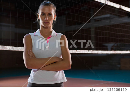 Female volleyball player standing arms crossed wearing polo on court showing net and court lines 135306139