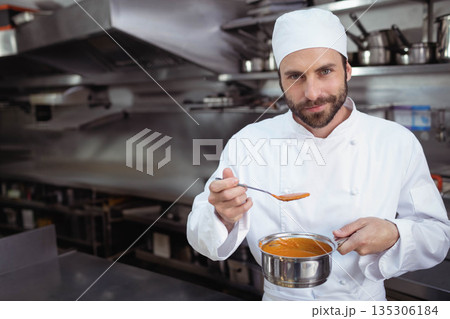 Professional male chef holding saucepan and tasting tomato soup in commercial kitchen, copy space 135306184