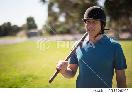 Senior male polo player posing on field wearing teal shirt, helmet while holding mallet, copy space Senior male polo player posing on field wearing teal shirt, helmet while holding mallet, copy space 135306205