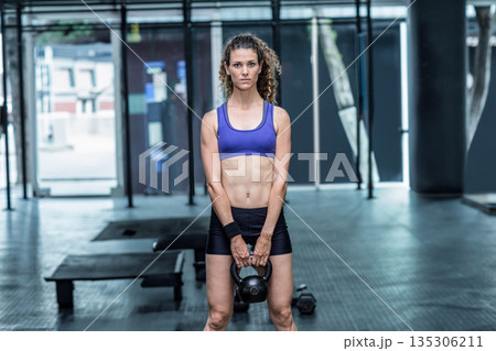 Female trainer in sportswear lifting black kettlebell in gym interior beside weight bench, dumbbell Female trainer in sportswear lifting black kettlebell in gym interior beside weight bench, dumbbell 135306211