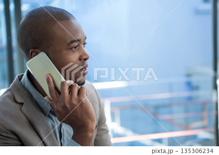 African American man in blazer holding smartphone to ear by glass railing in office, copy space 135306234