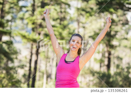 Woman in twenties stretching in sunlit forest wearing fuchsia tank top and black sports bra 135306261