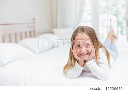 Female child smiling gently while lying on bed in bedroom under sheer curtains with white pillows Female child smiling gently while lying on bed in bedroom under sheer curtains with white pillows 135306264