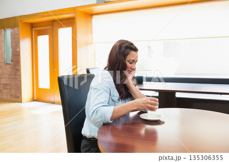 Woman holding white ceramic cup above saucer at table in cafe wearing denim shirt, copy space 135306355