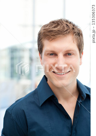 Man standing in office lobby wearing dark blue collared shirt near glass panels under natural light Man standing in office lobby wearing dark blue collared shirt near glass panels under natural light 135306373