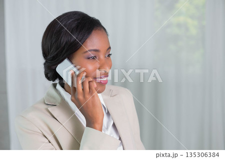 African American woman wearing beige blazer holding smartphone and speaking at office, copy space African American woman wearing beige blazer holding smartphone and speaking at office, copy space 135306384