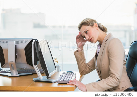 Female office worker wearing blazer leaning head on hand, typing on keyboard in office, copy space Female office worker wearing blazer leaning head on hand, typing on keyboard in office, copy space 135306400
