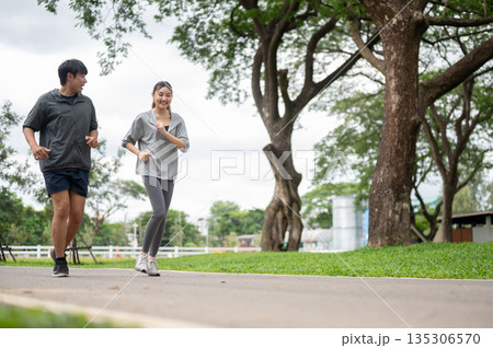Asian woman and man in sportswear smiling talking during run or jogging together on pavement in park Asian woman and man in sportswear smiling talking during run or jogging together on pavement in park 135306570