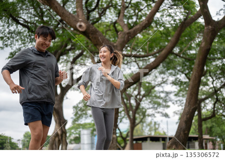 Asian man and a woman wearing sportswear laughing during a running or jogging on pavement in park. Asian man and a woman wearing sportswear laughing during a running or jogging on pavement in park. 135306572