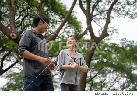 Asian man and woman in sportswear talking laughing at each other while running or jogging in park Asian man and woman in sportswear talking laughing at each other while running or jogging in park 135306573