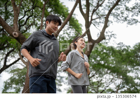 Asian man and woman in sportswear smiling as looking ahead while running or jogging together in park Asian man and woman in sportswear smiling as looking ahead while running or jogging together in park 135306574