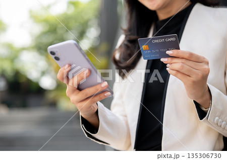 Close up of female office worker businesswoman holding phone and credit card while standing outside Close up of female office worker businesswoman holding phone and credit card while standing outside 135306730