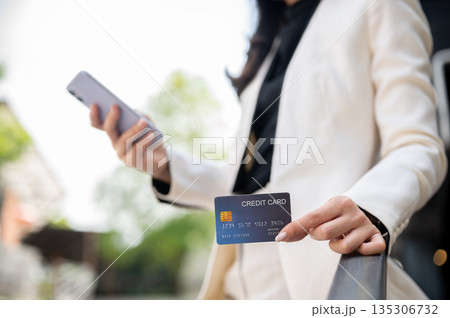 Close up of office worker or businesswoman holding phone showing credit card while standing outside. Close up of office worker or businesswoman holding phone showing credit card while standing outside. 135306732