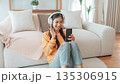 Asian woman listening to music with headphones and mobile phone in living room at home 135306915