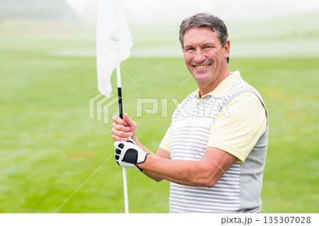 Senior African American man in polo standing on putting green holding flag beside hole, copy space Senior African American man in polo standing on putting green holding flag beside hole, copy space 135307028