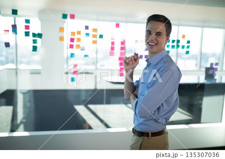 Adult man standing before glass partition with sticky notes near windows in office, copy space Adult man standing before glass partition with sticky notes near windows in office, copy space 135307036