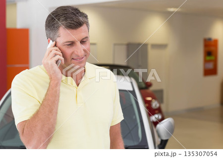 Senior man calling on smartphone and inspecting two-tone car with red panel in dealership showroom Senior man calling on smartphone and inspecting two-tone car with red panel in dealership showroom 135307054