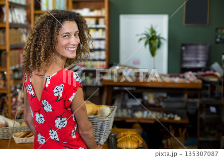 Woman holding basket with bread loaves in red floral dress behind counter at bakery, copy space Woman holding basket with bread loaves in red floral dress behind counter at bakery, copy space 135307087