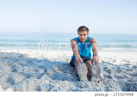 Male athlete stretching forward on shoreline, wearing sports watch and running shoes Male athlete stretching forward on shoreline, wearing sports watch and running shoes 135307098