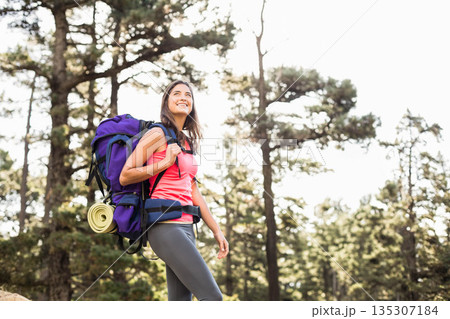 Female hiker standing on forest trail wearing coral tank with purple backpack and mat, copy space 135307184