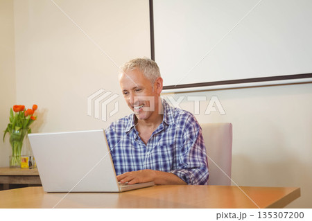 Man wearing plaid shirt typing on laptop at home workspace with wooden table and orange tulips Man wearing plaid shirt typing on laptop at home workspace with wooden table and orange tulips 135307200